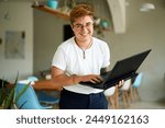 Smiling transgender professional holds laptop, works happily in modern office space. Inclusive workplace, young trans person enjoys career, experiences job fulfillment with tech in eco-friendly area.