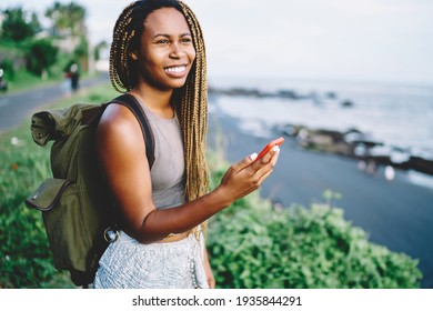 Smiling travel girl with mobile phone in hand enjoying summer vacations for exploring beautiful nature on vacations, millennial blogger with rucksack using cellular technology during wanderlust trip