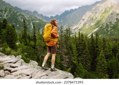 Smiling traveler with a bright backpack on a hiking mountain trail. A beautiful woman on a cliff enjoying the mountain scenery. Active lifestyle. - Powered by Shutterstock