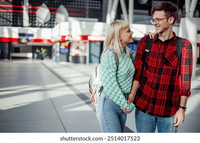 Smiling traveling couple hugging and holding hands at train station while waiting for their train. Loving urban couple looking forward to their journey. Trendy couple at metro station catching a train - Powered by Shutterstock