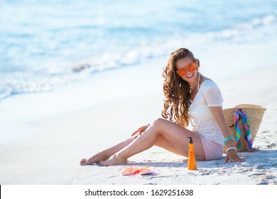 Smiling Trendy 40 Year Old Woman In White T-shirt And Pink Shorts With Long Wavy Hair Sitting On The Seacoast.