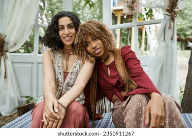 smiling and trendy multiethnic women in boho styled clothes spending time in patio in retreat center