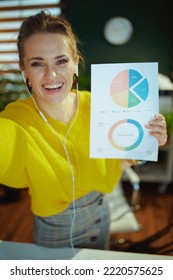 Smiling Trendy Small Business Owner Woman In Yellow Sweater In The Modern Green Office Having Video Chat And Showing Charts.