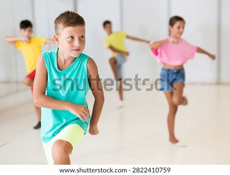 Smiling tween boy training movements of modern vigorous dance with group of children in choreographical studio.