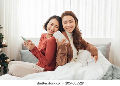 Smiling Two Asian young lovely couple repose on white bed and happy playing with smartphone and social media. - Shutterstock ID 2054335529
