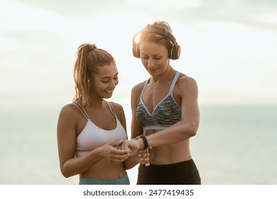 A smiling two women friends are looking at smartwatch and preparing to jogging in sunrise during summer beach holiday. - Powered by Shutterstock