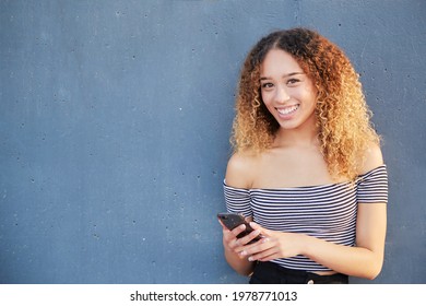 Smiling underage Latina girl holding smartphone using mobile app technology at home. Happy young Hispanic girl texting, checking social media apps. High quality photo