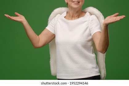 A Smiling Unrecognizable Older Woman In A White Blouse With White Angel Fur Wings. Hands Spread And Raised, With Palms Up. It Is A Gesture Of Arrangement And Openness. No Face. Green Background