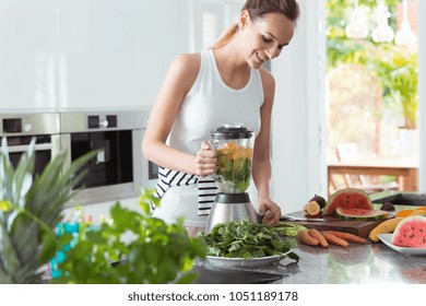 Smiling vegan woman making a smoothie with watermelon and carrots