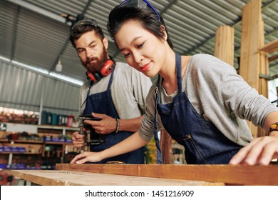 Smiling Vietnamese female carpenter working with wood under control of coworker - Powered by Shutterstock