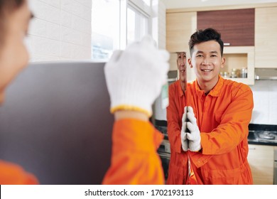 Smiling Vietnamese Moving Service Workers Transporting Refrigerator In Kitchen Of Customer