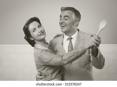 Smiling Vintage Couple Dancing In The Kitchen And Holding A Wooden Spoon