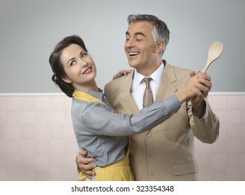 Smiling vintage couple dancing in the kitchen and holding a wooden spoon