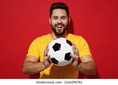 Smiling vivid fun young bearded man football fan in yellow t-shirt cheer up support favorite team look camera hold in hands give you soccer ball isolated on plain dark red background studio portrait - Powered by Shutterstock