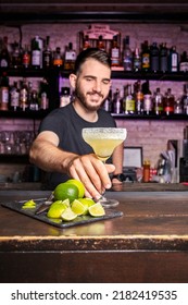 Smiling Waiter Leaving A Cocktail Above The Bar Counter. Vertical