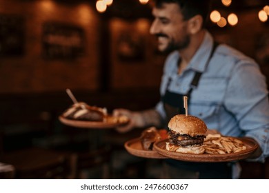 Smiling waiter in the restaurant serving two plates of burgers. Focus on a burger on plate - Powered by Shutterstock