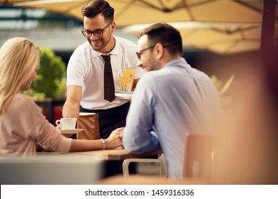 Smiling waiter serving coffee to a couple in a cafe.  - Powered by Shutterstock