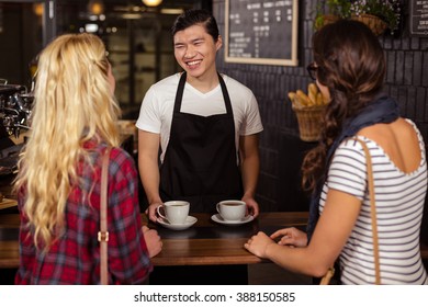 Lächelnder Kellner, der den Kunden im Café einen Kaffee serviert
