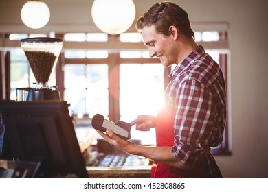 Smiling waiter standing at counter using credit card machine