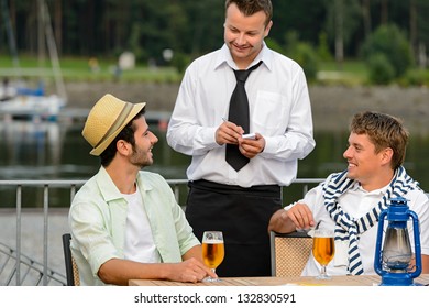Smiling waiter taking order from men customers outdoor bar