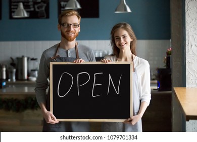 Smiling waiter and waitress holding chalkboard with open sign, cafe or coffee shop house business owners partners looking at camera welcoming inviting advertising new cafeteria bistro bar, portrait - Powered by Shutterstock