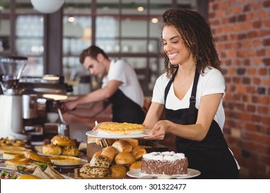 Smiling Waitress Holding Cake In Front Of Colleague At Coffee Shop