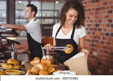 Smiling waitress putting bread roll in paper bag at coffee shop - Powered by Shutterstock