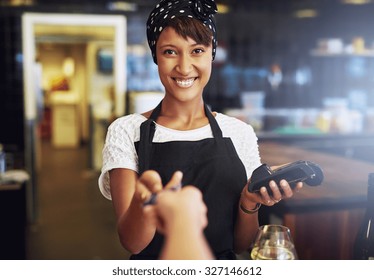 Smiling Waitress Or Small Business Owner Taking A Credit Card From A Customer To Process Through The Banking Machine In Payment For An Order