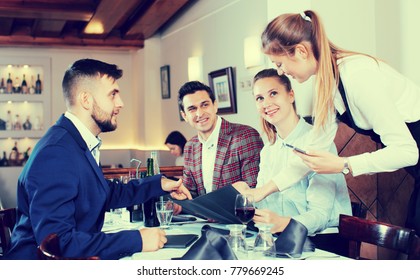 Smiling waitress taking order from guests, using digital tablet