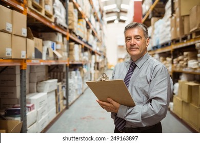 Smiling warehouse manager holding a clipboard in a large warehouse - Powered by Shutterstock