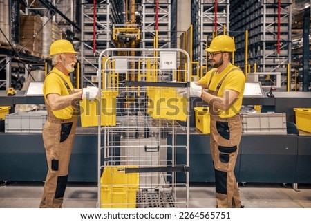 Smiling warehouse workers preparing a shipment in a large warehouse.Warehouse workers talking about logistics and distribution.