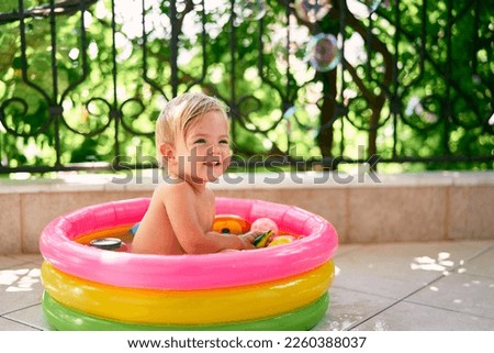 Smiling wet child sitting in a small inflatable pool with toys