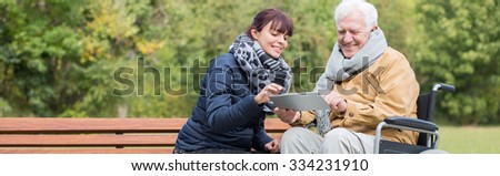 Smiling wheelchair man is using tablet outdoor