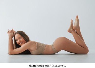 Smiling when lying down on the floor. Woman in underwear with slim body type is posing in the studio.
