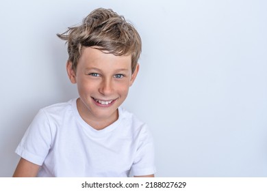 Smiling White Eastern European Boy 9 Years Old During A Holiday. Portrait Of A Boy In A White T-shirt On A Gray Background.