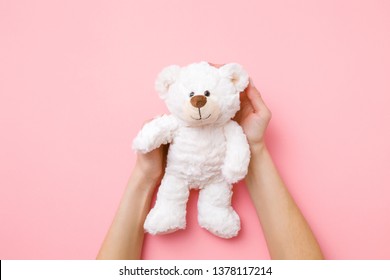 Smiling white teddy bear in girl hands on pastel pink background. Kids best friend. Point of view shot.