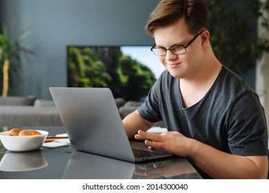 Smiling white young man with down syndrome using laptop computer at home sitting at the table