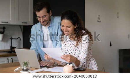 Smiling wife satisfied husband manage family budget, use laptop e-bank app, happy spouses reading received paper letter about loan repayment, learn bank account print out, financial success concept