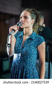 Smiling And Witty Female Stand Up Actor Comedian On Stage, Talking And Singing Into A Microphone And Making The Audience Laugh. Final Rehearsal Before The Premiere And Performance In The Theater