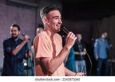 Smiling And Witty Stand Up Actor Comedian On Stage, Talking And Singing Into A Microphone And Making The Audience Laugh. Final Rehearsal Before The Premiere And Performance In The Theater