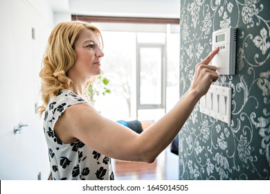 A Smiling Woman Adjusting Thermostat On Home Heating System