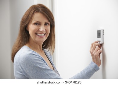 Smiling Woman Adjusting Thermostat On Home Heating System