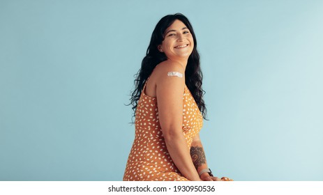 Smiling woman after getting vaccine on blue background. Happy woman showing her arm with bandage after receiving vaccination. - Powered by Shutterstock