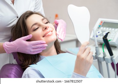 Smiling woman after teeth whitening procedure looking at mirror, caries treatment, toothache elimination. Pretty happy girl at stomatologist appointment in dental clinic