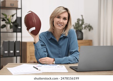 Smiling woman with american football ball at table in office - Powered by Shutterstock