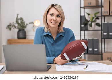 Smiling woman with american football ball at table in office - Powered by Shutterstock