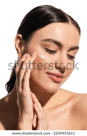 smiling woman applying moisturizing face cream on cheek isolated on white