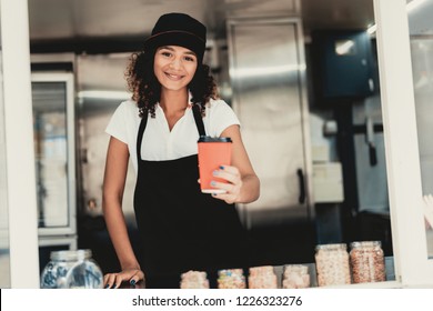 Smiling Woman In Apron Standing In Food Truck. Cup Of Coffee. Street Food Concept. Food In Town. Selling Snacks. Girl In Cap. Black Arpon. Working Outdoor. Woman In Shirt. Standing Girl.