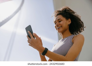 Smiling woman athlete in sportswear standing outdoors after training and use mobile phone - Powered by Shutterstock