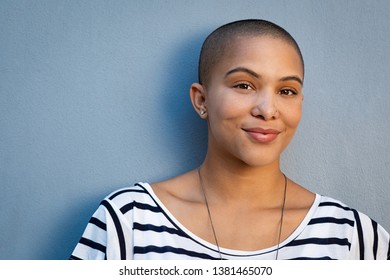 Smiling woman with bald hair looking at camera. African american woman in white and black stripe shirt standing isolated against blue background. Closeup face of proud and satisfied cool girl. 